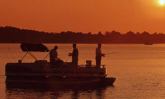 A group of fishermen holds their lines as the sun shines golden in the distance.